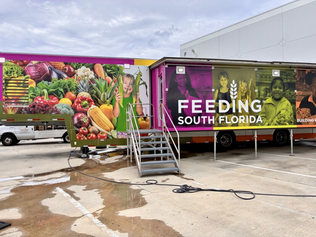 Feeding South Florida trailer wrapped with colorful produce graphics, portraits of children, and large white organization lettering by DNA Marketing & Printing